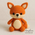 Handmade amigurumi fox doll in vibrant orange and cream colors, crocheted with fine yarn, sitting upright with a cute expression – perfect for woodland nursery decor or crochet pattern inspiration by AmyLiva Handmade.